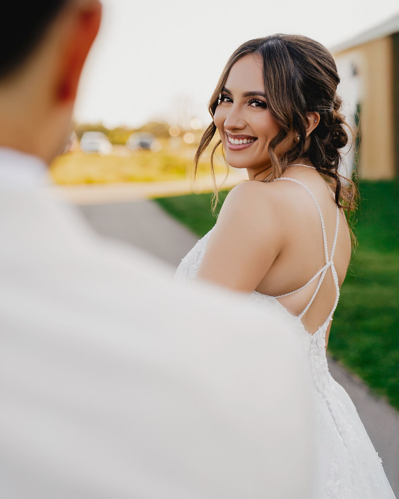 Smiling bride in a lace gown with thin beaded straps glancing back over her shoulder at her groom, Minnesota wedding
