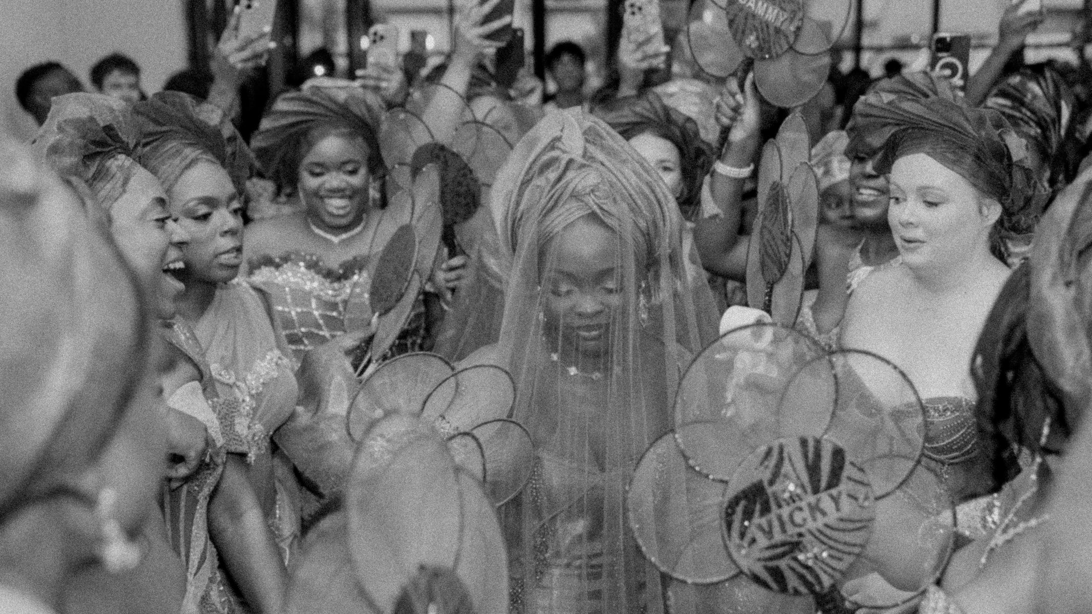 Black and white photo of a bride in a veil surrounded by a celebrating crowd