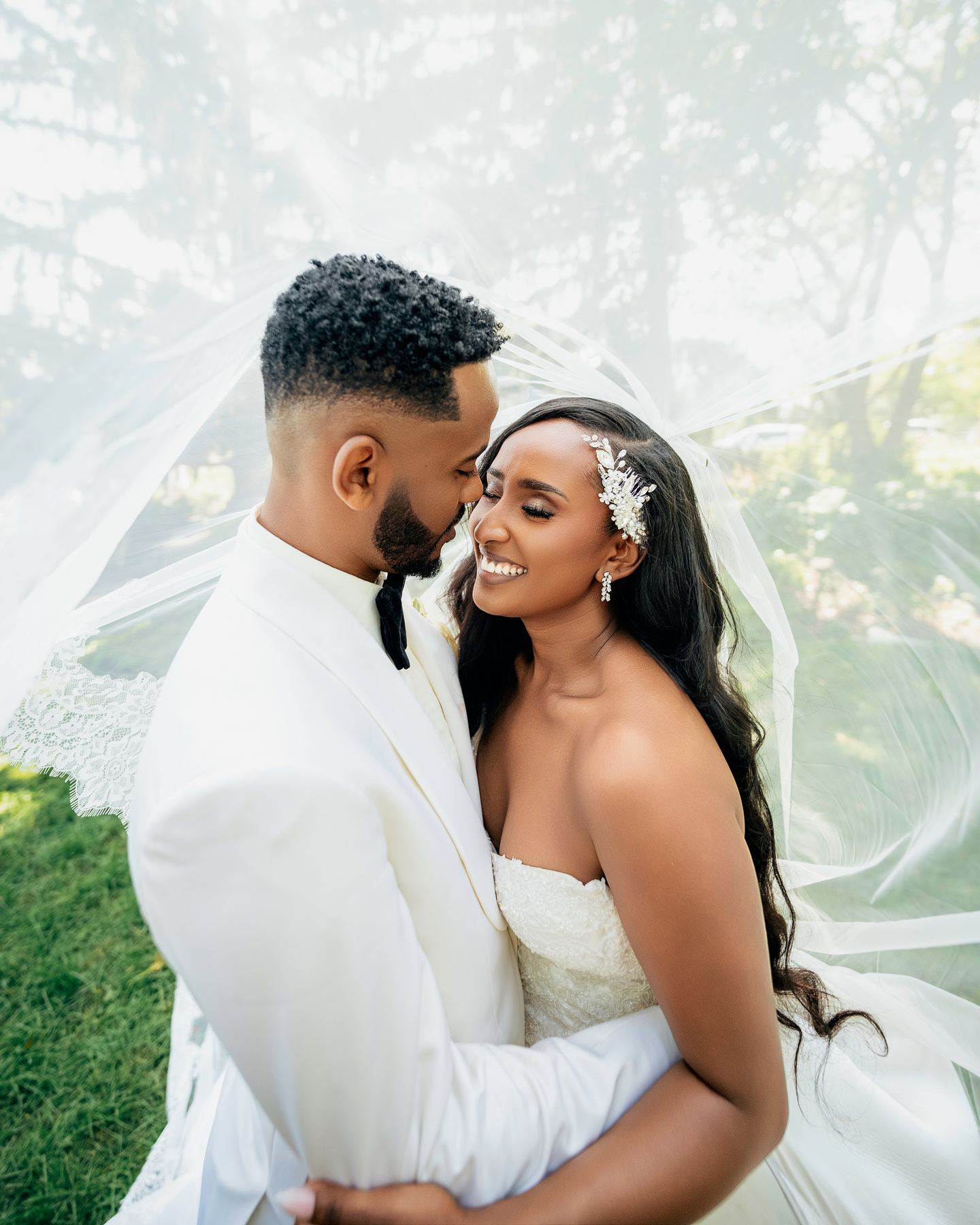Groom kissing bride's forehead outdoors while she holds her veil