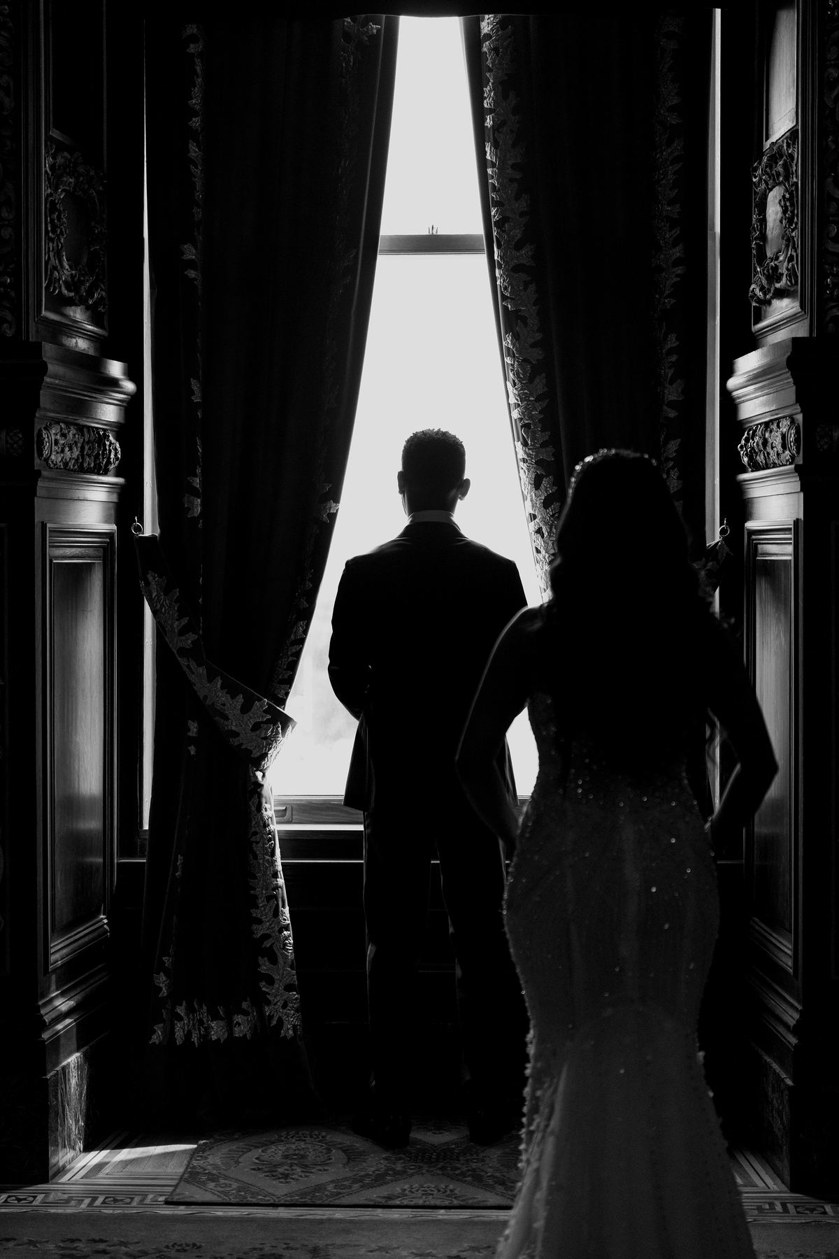 Silhouette of bride and groom looking out a window, black and white