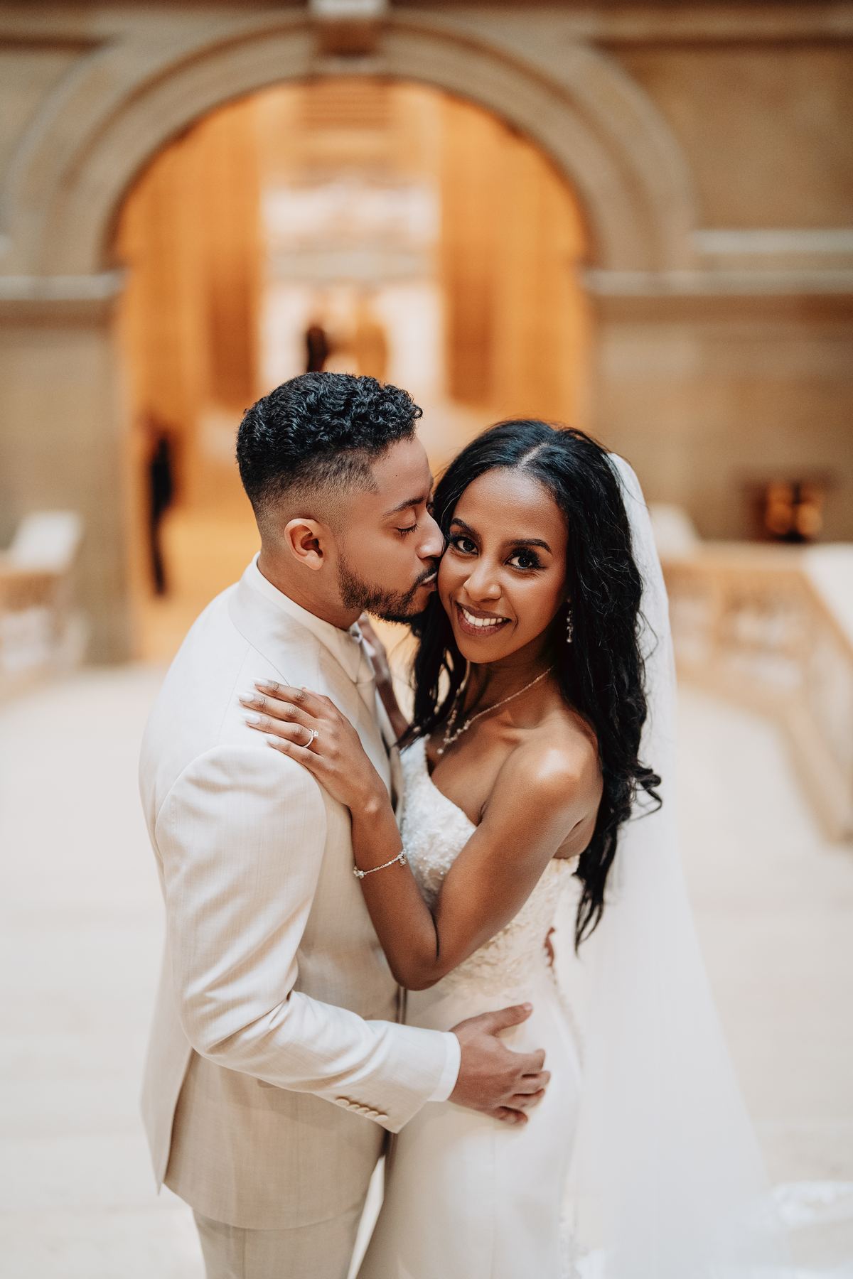 Groom kissing bride's cheek in front of an arched museum window