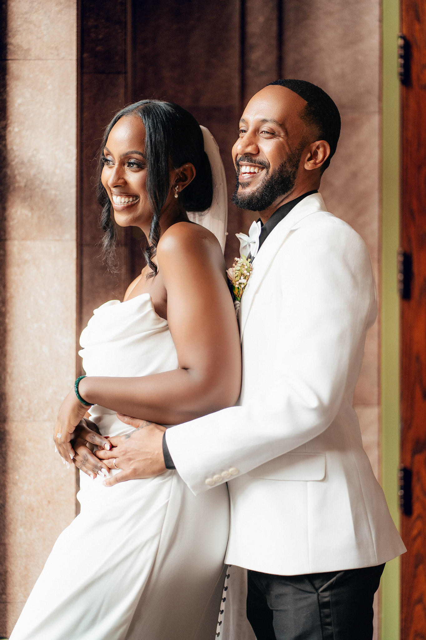 Laughing bride and groom in white embracing by a stone wall at Union Depot in St. Paul, Minnesota wedding